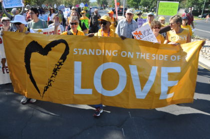 UU community marches with sign "Standing on the Side of Love"
